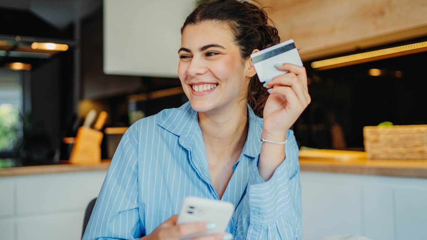 Frugal Gen Z Habits People Make Fun Of But Actually Work Gen Z woman smiling and holding up a credit card.