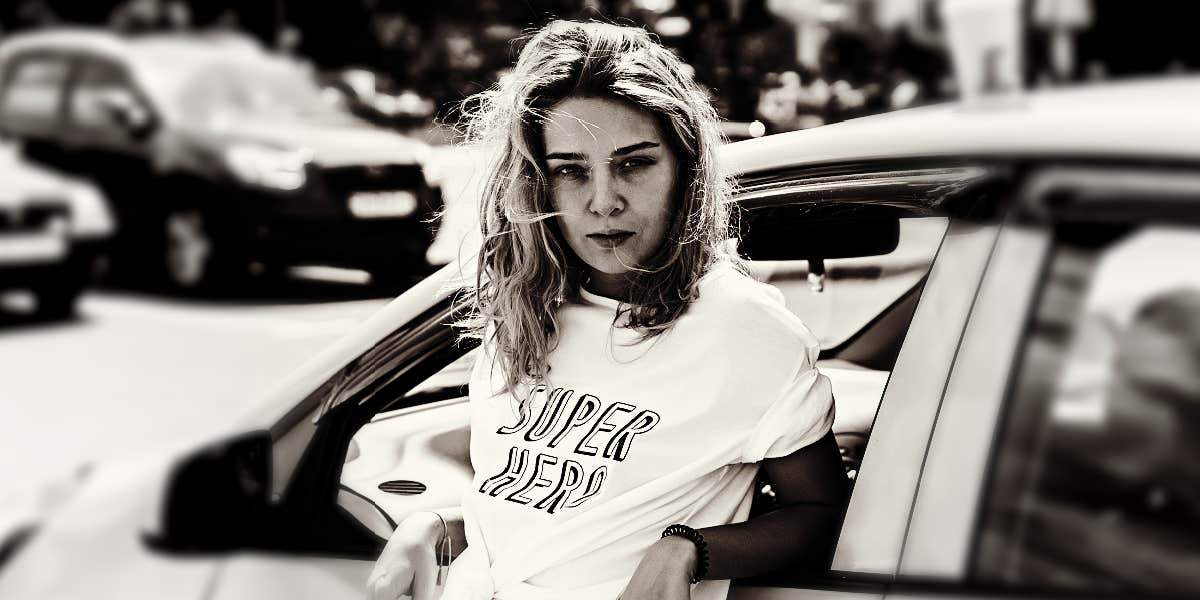 Sign that long-term anger has taken over young woman with an angry expression leans back against a car in the city